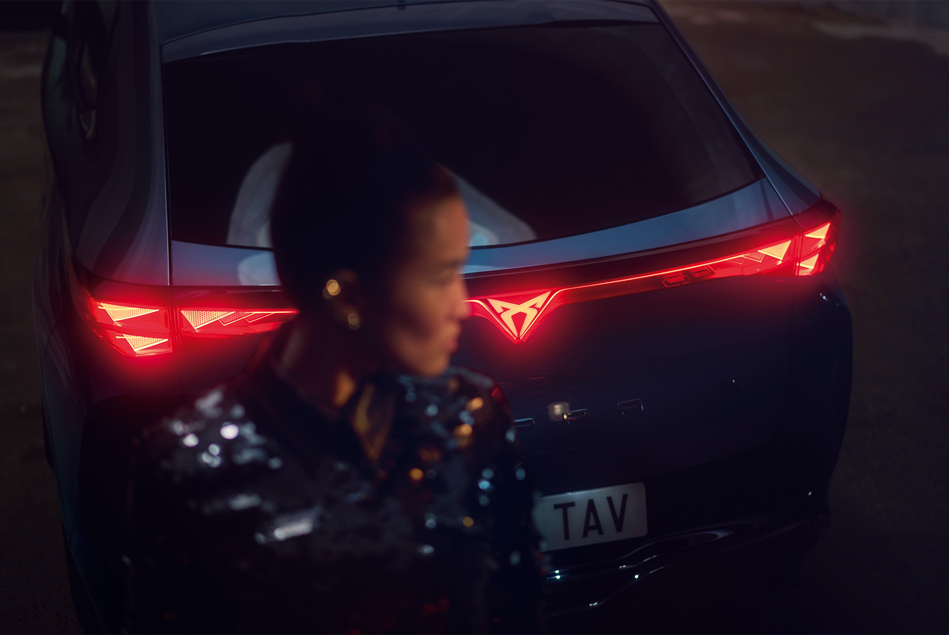 New CUPRA Tavascan rear lighting with woman standing behind car, blurry face.