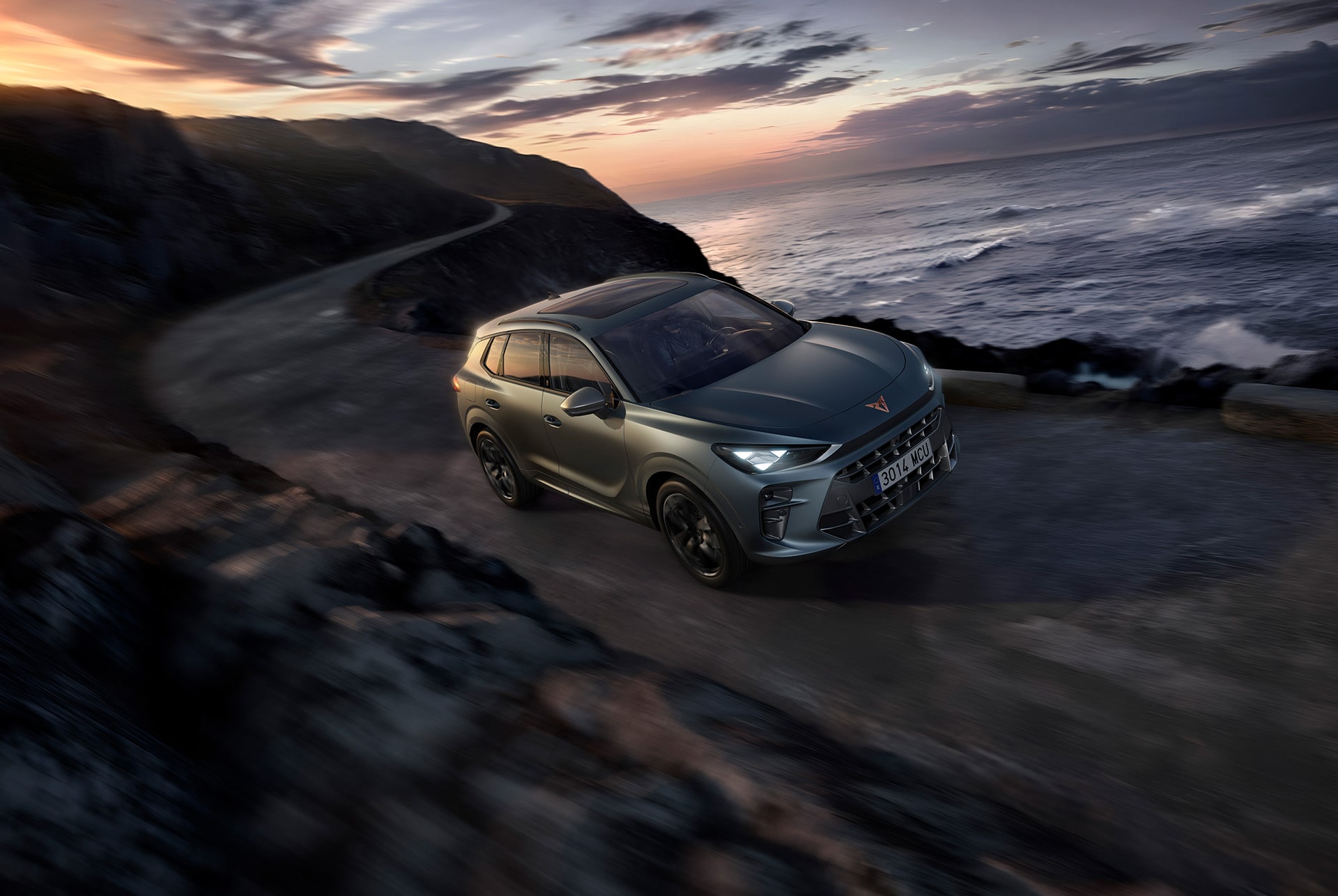 cupra terramar, america’s cup exclusive version, enceladus grey matt, featuring 20 inch america’s cup alloy wheels, cupra matrix led ultra hd headlights, and dynamic chassis control (dcc), driving on a wet winding road by the sea at sunset.